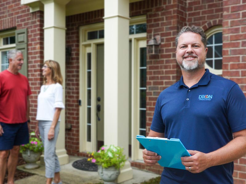 A Dixon Painting expert is standing outside a house while a couple chats in the background in Marietta, GA