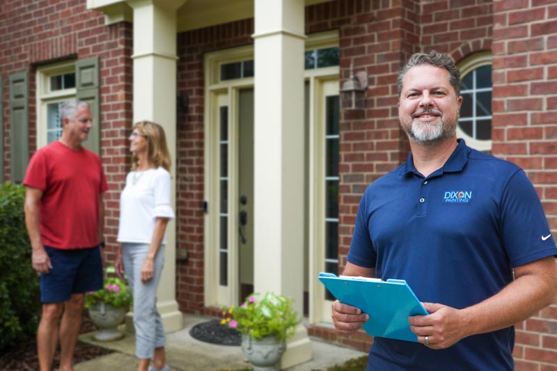 Dixon Painting expert with a smile, standing by a brick house, with a couple chatting in the background in Atlanta, GA.