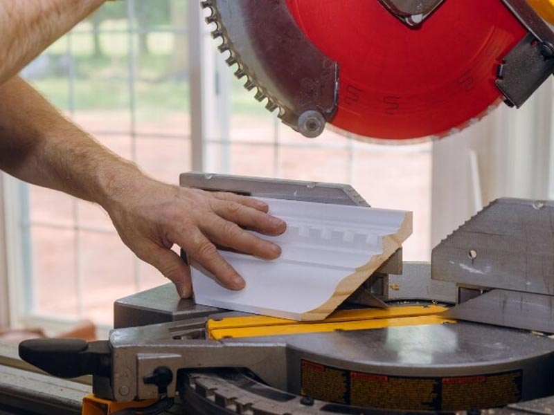 Man skillfully cutting crown molding with a precise machine saw in Atlanta - Dixon Painting