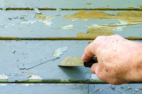 Man's hand shown scraping old gray paint from deck